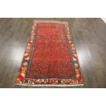 A North West Persian Woollen Rug with an all over foliate design upon a red ground within multiple
