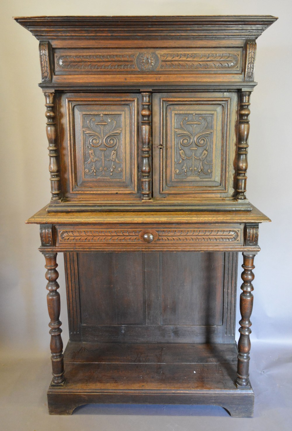 An Oak Cabinet on Stand, the moulded cornice above two carved doors flanked by turned pilasters,