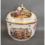 A German Porcelain Large Covered Tureen with Hand Painted Reserves and mounted with Two Figures,