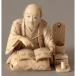 A SIGNED JAPANESE MEIJI PERIOD IVORY OKIMONO OF A STREET SCRIBE, kneeling with an open book and with