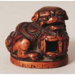 A JAPANESE EDO/MEIJI PERIOD CARVED WOOD NETSUKE OF A SHI-SHI LION DOG, its head resting on a pierced