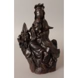 A 19TH CENTURY CHINESE BROWN GLAZED STONEWARE FIGURE OF GUANYIN, seated on a rocky plinth with an