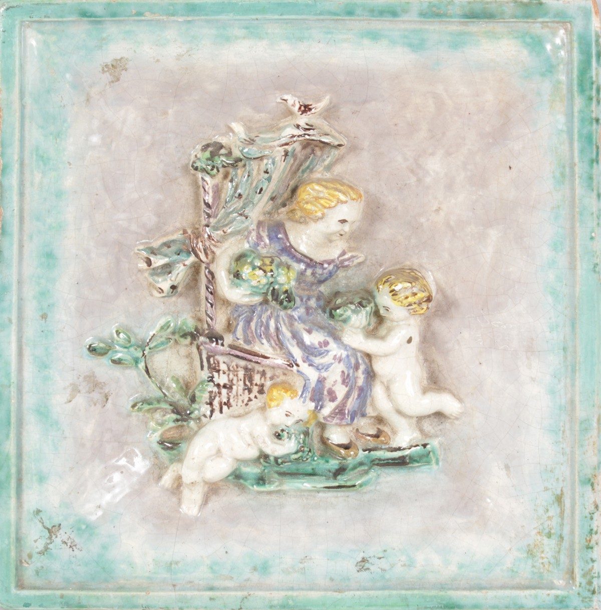 A FAIENCE SQUARE COLOURED TILE, a lady on a chair with two cupids in relief. 11ins x 10ins.