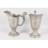 A PAIR OF PEWTER PEDESTAL EWERS with scrolling handles, on circular bases. 9.5ins high.