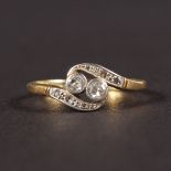 AN 18CT YELLOW GOLD TWO STONE DIAMOND CROSSOVER RING.