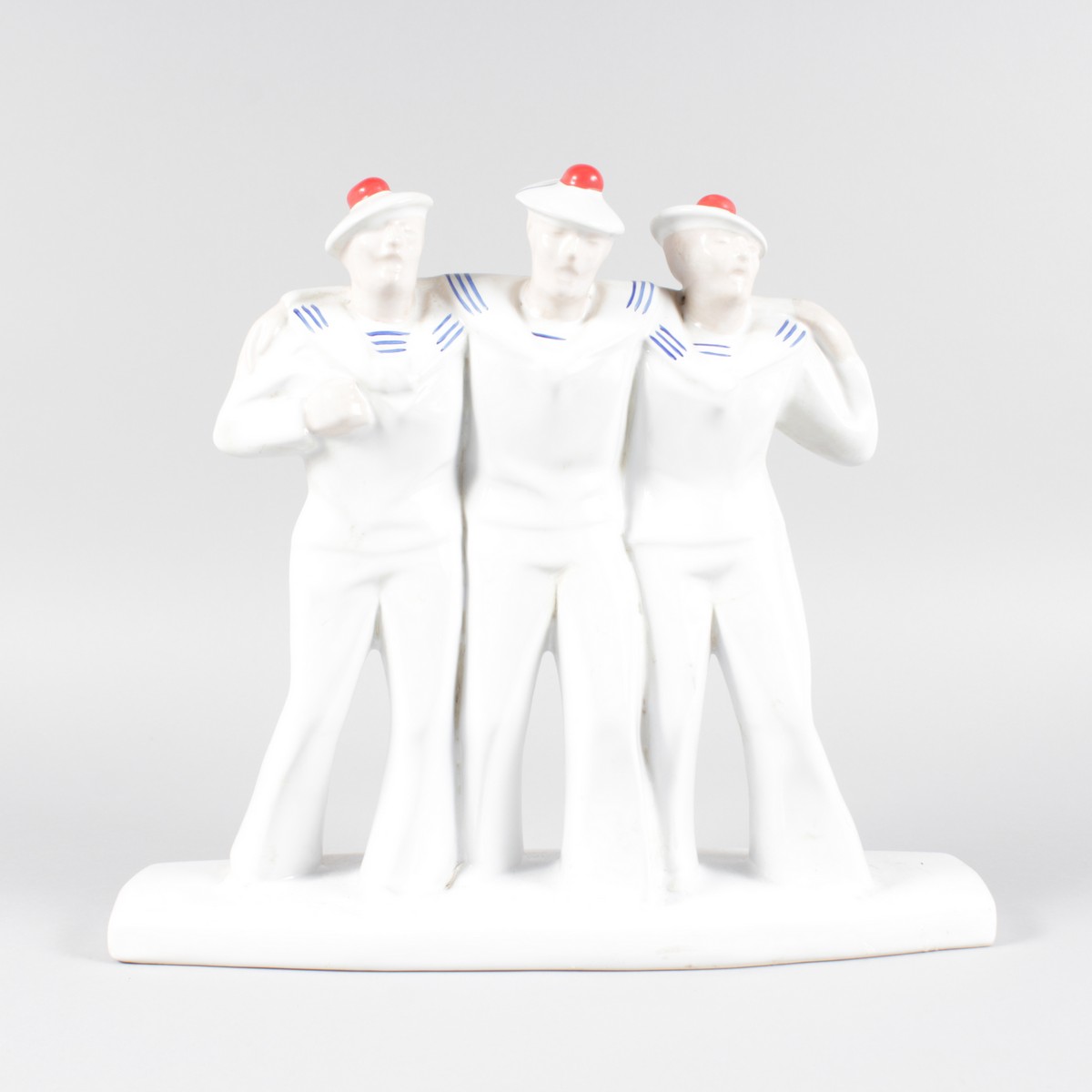 AN ART DECO DESIGN BLUE AND WHITE GROUP OF THREE SAILORS with red pom pom hats. 11ins high.