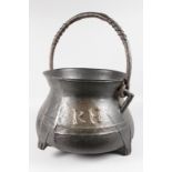 A LARGE EARLY BRONZE CAULDRON, initialled RH, with swing handle, on four legs. 14ins diameter.