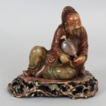 A CHINESE STAINED SOAPSTONE FIGURE OF A RECLINING SAGE, together with a pierced soapstone stand, 5.