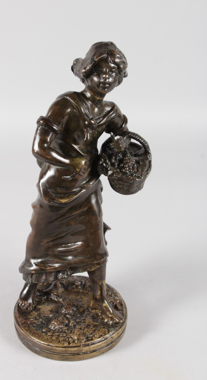 A 19TH CENTURY FRENCH BRONZE OF A YOUNG WOMAN carrying a basket of fruit and standing on a