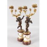 A SUPERB PAIR OF REGENCY BRONZE, ORMOLU AND MARBLE CUPID CANDLESTICKS on pedestals, formed as cupids
