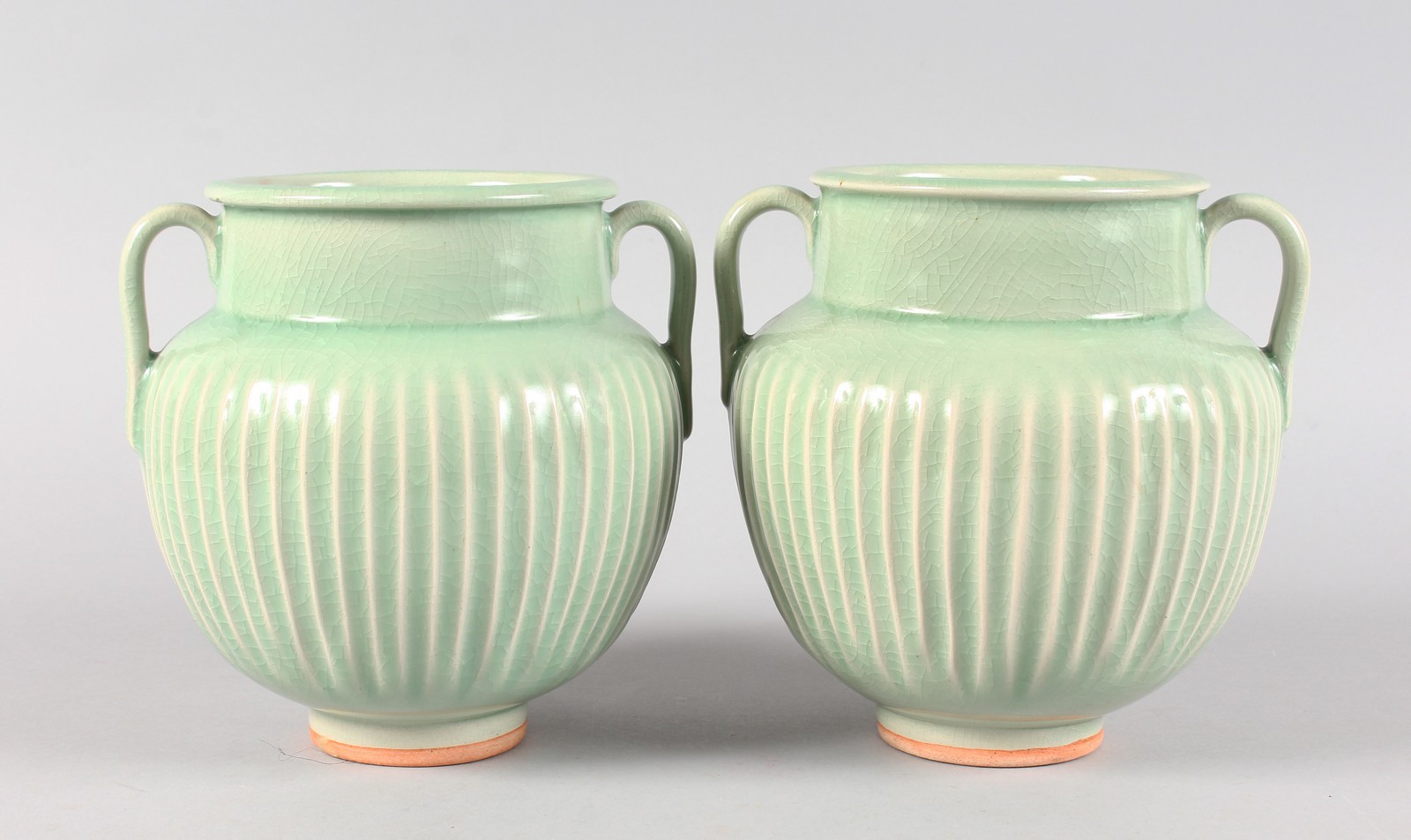 A PAIR OF GREEN FLUTED TWO HANDLED BULBOUS VASES. 7.5ins high.