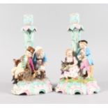 A PAIR OF AUGUSTUS REX PORCELAIN CANDLESTICKS, the bases with children and a goat. Mark in blue.