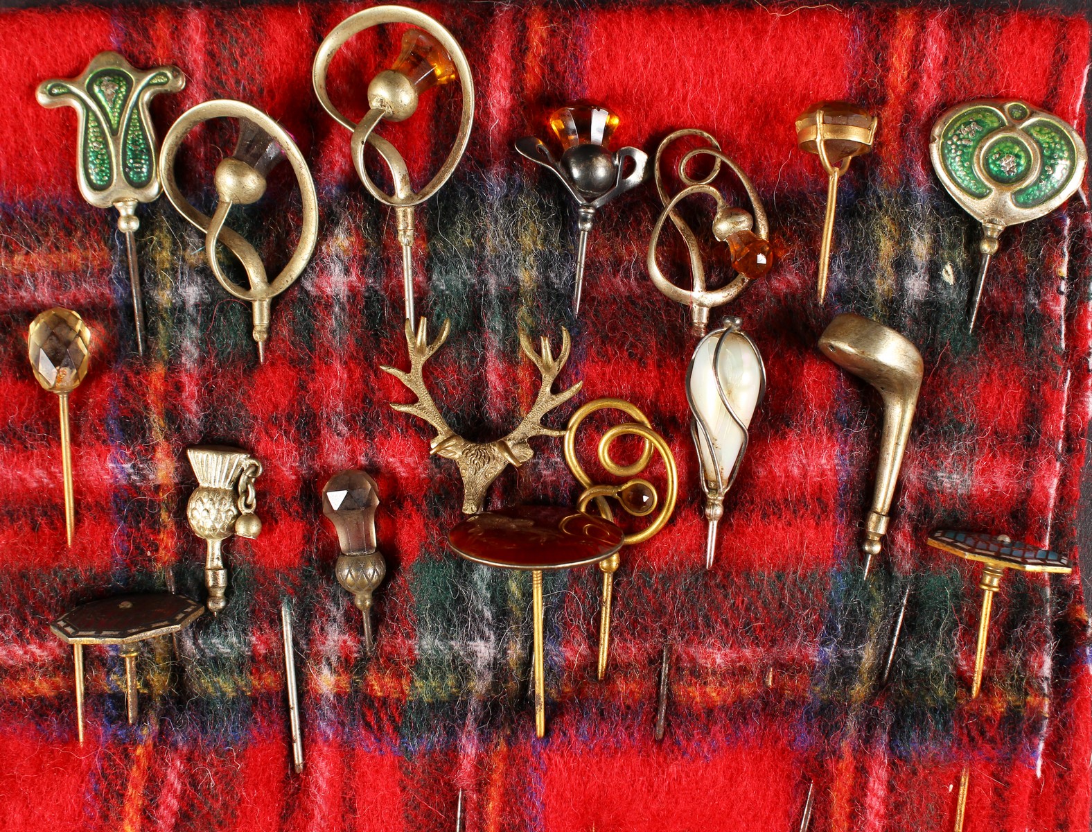 A COLLECTION OF SEVENTEEN VICTORIAN AND EDWARDIAN HAT PINS on a tartan cloth.