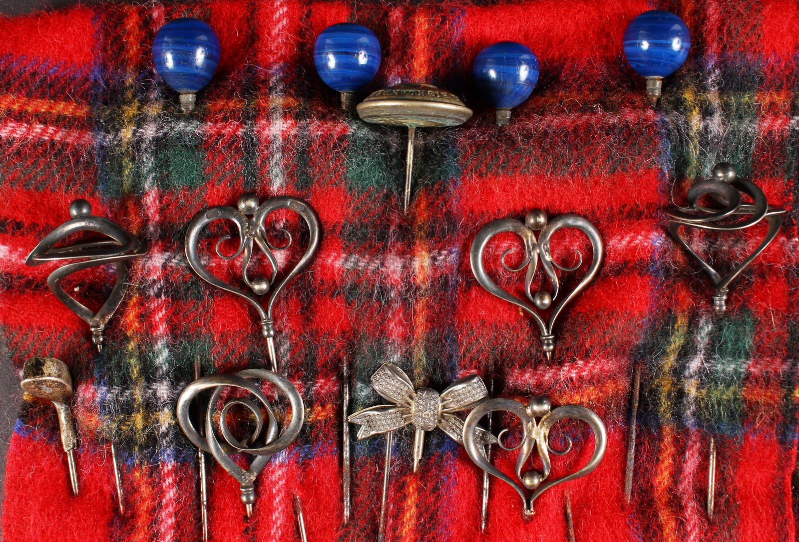 A COLLECTION OF FOURTEEN VICTORIAN AND EDWARDIAN HAT PINS on a tartan cloth.