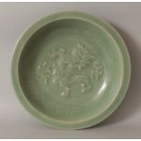 A LARGE MING STYLE LONGQUAN MOULDED CELADON DISH, the interior decorated with a dragon, 13.8in