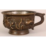 A CHINESE MING STYLE BRONZE CUP, with a scroll handle, the sides cast in high relief with a