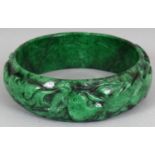 A CHINESE JADE BANGLE, carved to the rounded rim with foliage, the green stone with black