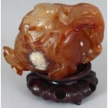 A CHINESE AGATE CARVING OF A FROG RESTING ON TOP OF A POMEGRANATE, together with a wood stand, the