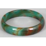 A CHINESE JADE LIKE GLASS BANGLE, of striated green and russet colouring, 3in diameter, the inner