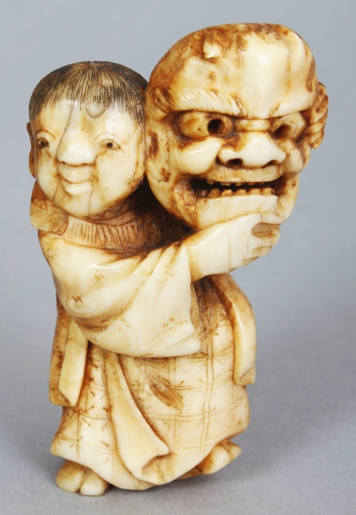 A JAPANESE MEIJI PERIOD IVORY NETSUKE OF A STANDING BOY, unsigned, the boy bearing aloft a Noh mask,