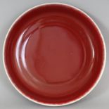 A CHINESE COPPER RED PORCELAIN DISH, the glaze thinning at the rim, the base with a six-character