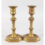 A PAIR OF EARLY BRASS CANDLESTICKS with square bases with cut off corners. 7.5ins high.