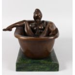 AN EROTIC BRONZE OF A YOUNG LADY IN A BATH, standing on a marble base. 12ins long.