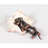 A PAINTED COLD CAST BRONZE DOG ON A PILLOW. 2.5ins.