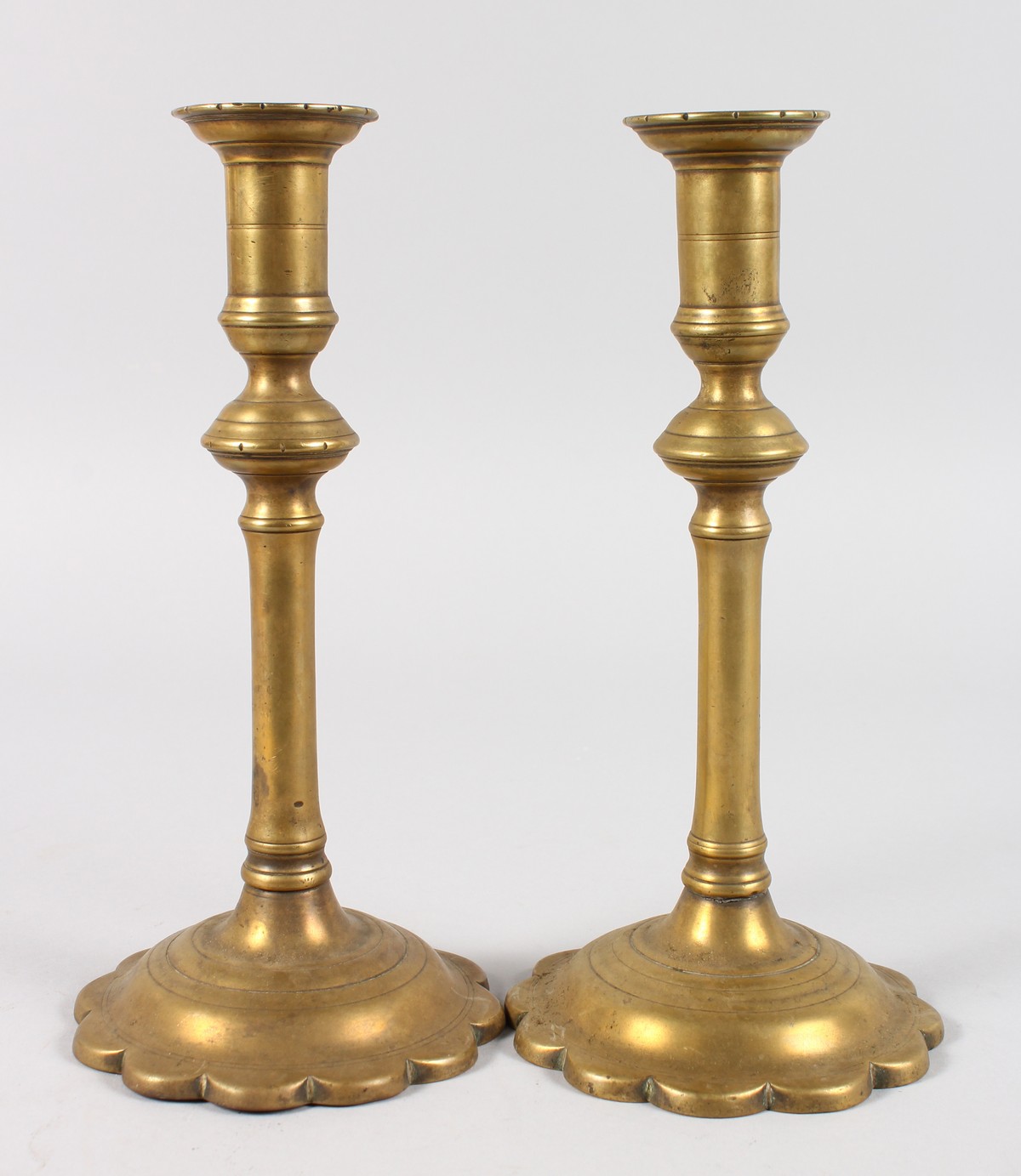 A PAIR OF EARLY PETAL BASE BRASS CANDLESTICKS. 9.25ins high.