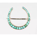 A SILVER AND TURQUOISE HORSESHOE BROOCH.