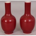 A PAIR OF CHINESE COPPER RED PORCELAIN BOTTLE VASES, each applied with an even and slightly