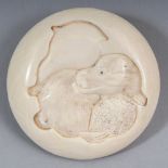 A SIGNED JAPANESE MEIJI PERIOD IVORY MANJU NETSUKE, carved to one surface with a seated puppy