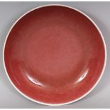 A CHINESE COPPER RED PORCELAIN SAUCER DISH, applied with a slightly mottled glaze thinning to