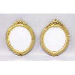 A SMALL PAIR OF GILDED OVAL MIRRORS with floral and bead decoration. 1ft 5ins long, 1ft wide.