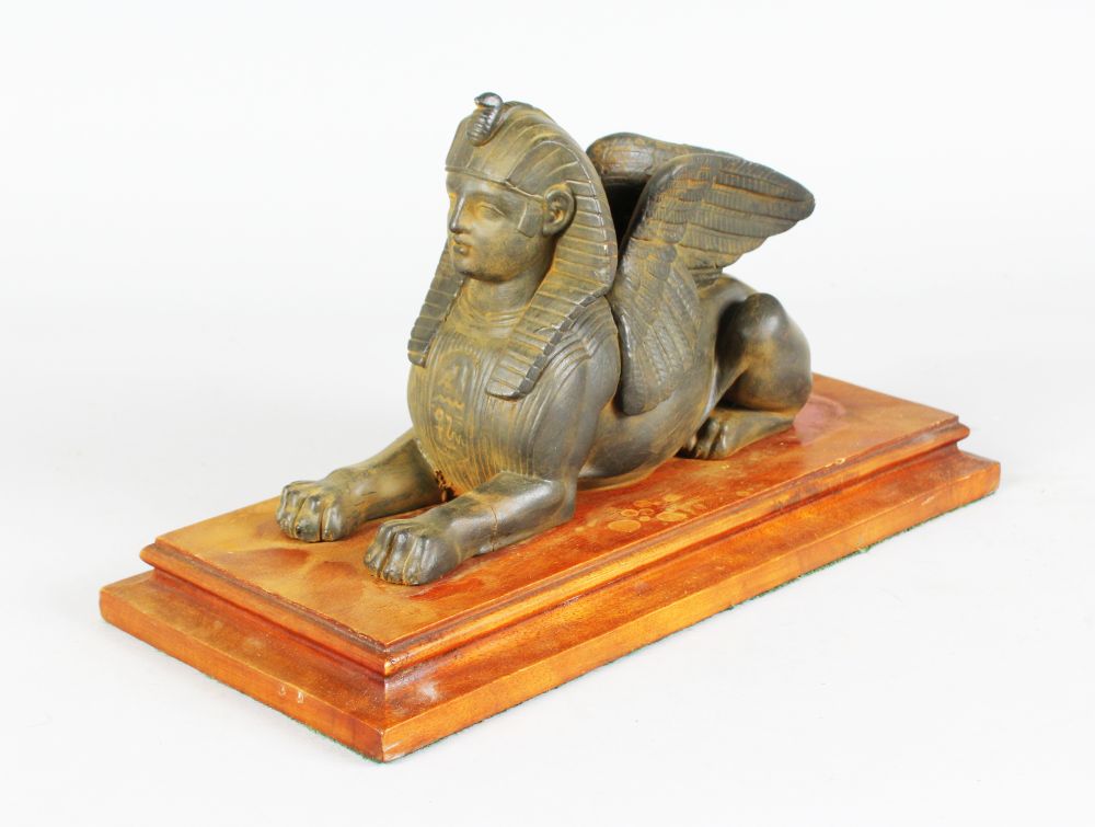 AN EGYPTIAN SPHINX on a mahogany base. 13ins long.