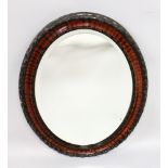 A MAHOGANY OVAL MIRROR in a plain and carved frame. 2ft 10ins long x 2ft wide.