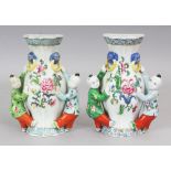 A PAIR OF CHINESE FAMILLE ROSE PORCELAIN WALL VASES, each moulded in the form of two boys supporting