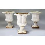 A GOOD SET OF THREE CAST IRON PEDESTAL URNS, white painted of Campana form. 1ft 8ins high.
