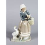 A LLADRO PORCELAIN FIGURE OF A YOUNG GOOSE GIRL, one in a basket on her arm. 9ins high.