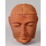 A CHINESE RED STONEWARE STYLE HEAD OF BUDDHA, modelled in an archaic manner, 11in high.