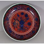 A CHINESE MING STYLE RED GROUND BLUE & WHITE LOTUS BOUQUET PORCELAIN SAUCER DISH, the rim with a