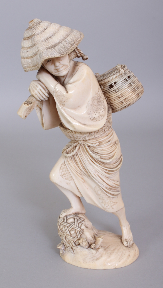 A GOOD QUALITY SIGNED JAPANESE MEIJI PERIOD IVORY OKIMONO OF AN ARTISAN, standing on rockwork and