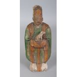 A CHINESE TANG STYLE GLAZED CERAMIC FIGURE OF A STANDING ATTENDANT, bearing a dog in his arms, the