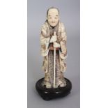 A FINE QUALITY JAPANESE MEIJI PERIOD IVORY OKIMONO OF A STANDING MAN, together with a fixed wood