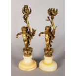 A PAIR OF FRENCH ORMOLU CUPID CANDLESTICKS, both playing violins and standing on onyx bases. 12.5ins