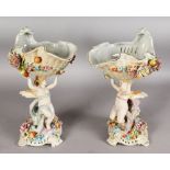 A PAIR OF DRESDEN STYLE PORCELAIN COMPORTS, modelled as cherubs holding aloft a shell decorated with