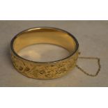 An ornately decorated 9ct gold bangle with safety chain, total approx weight 31.