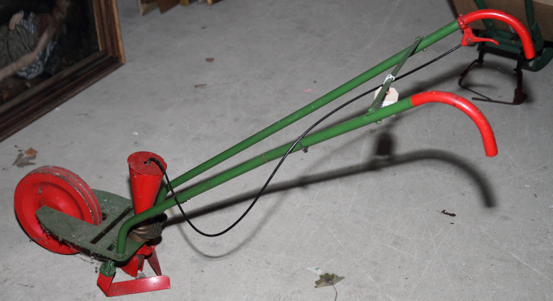 A red and green painted metal pea seed drill (purchased by Mr Snelson between 1890 and 1900 and used