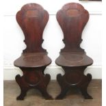 A pair of mid 18th Century mahogany hall chairs of William Kent design with panel seats, on splay