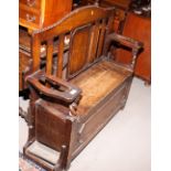 An early 20th Century oak hall bench with box seat and umbrella holders to arms, 45" wide